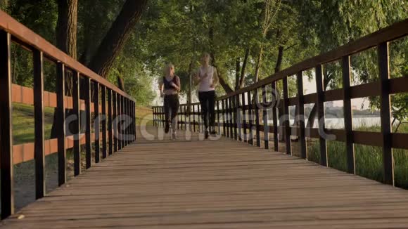 两位年轻漂亮的女跑步者扎着马尾辫在公园跨桥慢跑减肥健身模特跑步视频的预览图