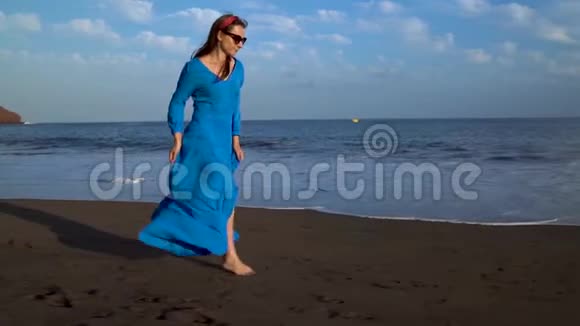 穿着蓝色裙子的女人沿着黑色火山海滩奔跑慢动作视频的预览图