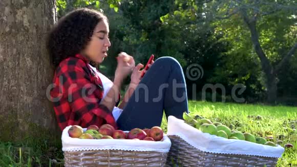 美国黑人混血少女少女在果园里靠在树上吃苹果视频的预览图