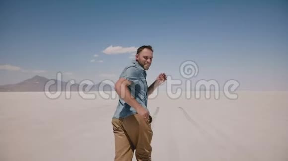 镜头跟随年轻快乐的自由男子向前奔跑张开双臂回首相机在犹他州的盐漠湖视频的预览图