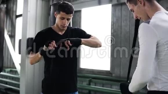 强壮的男人用黑色的运动绷带包裹双手两个人正在用拳击包包裹手准备训练和视频的预览图