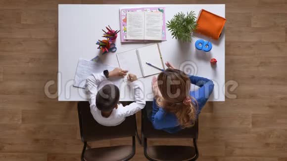 年轻的母亲帮儿子学习小男孩从笔记本上擦掉一些东西坐在桌子后面孩子在做视频的预览图
