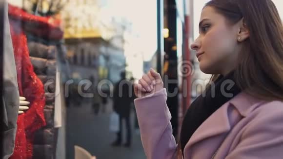 悲伤的女孩在商店橱窗里寻找梦想着昂贵的衣服销售和折扣视频的预览图