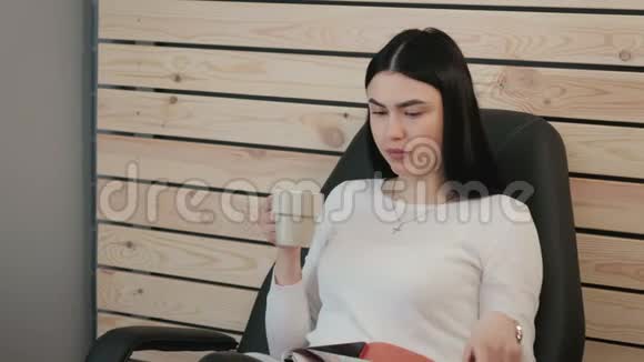 年轻的商务女士在办公室里喝咖啡翻阅杂志视频的预览图