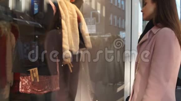 女学生伤心地看着昂贵的衣服在精品店橱窗购物视频的预览图