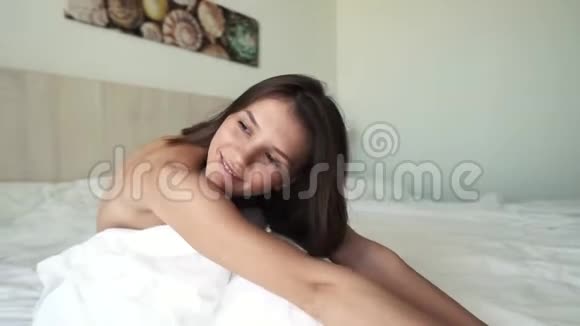 一个年轻漂亮的黑发女孩在床上醒来女孩躺在一张白色的床上空中观景4k决议视频的预览图