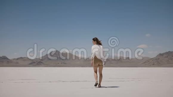 一个美丽的年轻快乐的女人在犹他州的盐漠湖上张开双臂看着镜头旋转视频的预览图