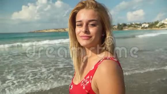 一幅金发的年轻女子站在海滩上穿着红色连衣裙近在咫尺可爱的女孩花时间在海边视频的预览图