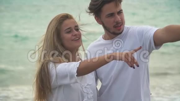 幸福的夫妇站在岩石海岸用手指缓慢地指着穿着白色衣服的男人和女人视频的预览图
