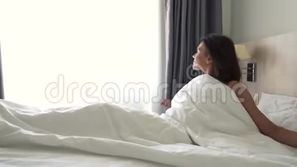 一个年轻漂亮的黑发女孩在床上醒来女孩躺在一张白色的床上空中观景4k决议视频的预览图