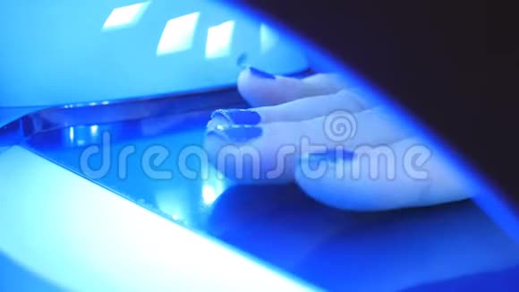 一个年轻的女人用一台特殊的机器在美甲沙龙里擦干指甲凝胶在紫外线下抛光视频的预览图