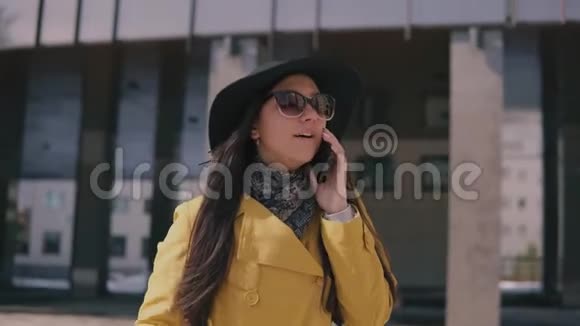 穿着黄色雨衣帽和眼镜的时髦女孩在电话里谈笑风生视频的预览图