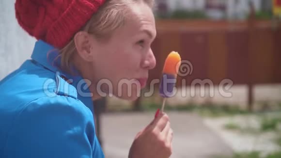 有趣的女孩在夏天吃冰淇淋金发女郎很有趣穿着一件蓝色的外套夏天戴着一顶红色的帽子幽默视频的预览图