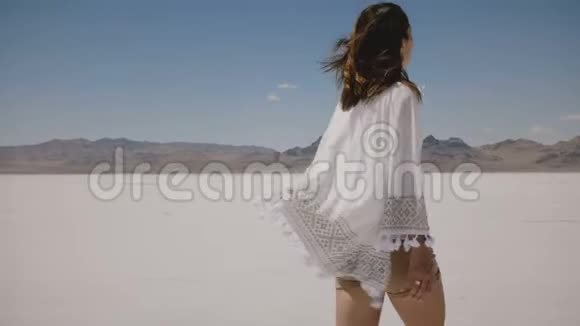 镜头跟随美丽快乐的自由女人在炎热的夏天沿着阳光明媚的犹他州盐漠湖散步转弯和摆姿势视频的预览图