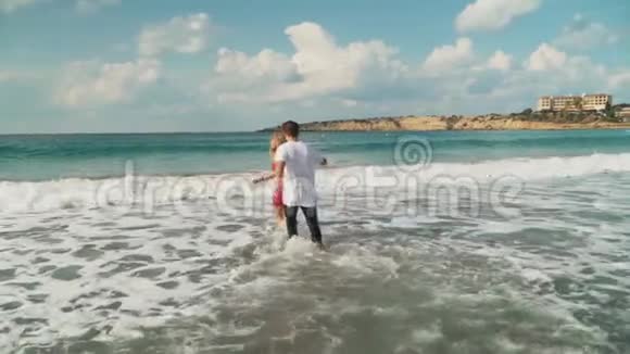 穿衣服的男人和女人缓慢地进入浅水快乐的一对夫妇要在波浪中游泳年轻人的休闲视频的预览图