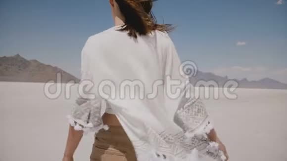 镜头跟随年轻快乐的美丽女人向前走风吹着衣服和头发在盐漠湖视频的预览图