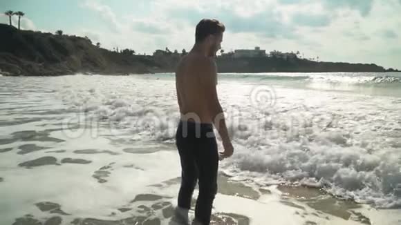 站在海浪前半裸的运动男子在风景如画的美丽海滩上感受自由视频的预览图