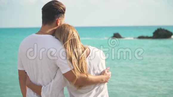 年轻的幸福夫妇站在海滨笑着拥抱着看着风景如画的海面慢动作视频的预览图