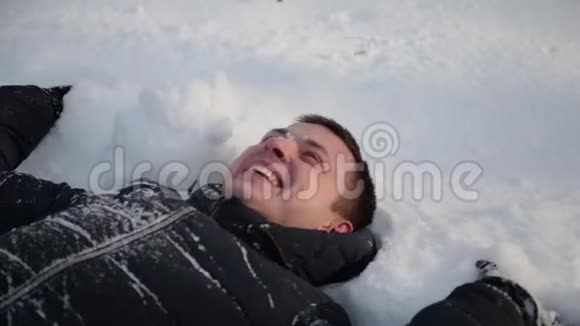 英俊的年轻人躺在雪地里微笑城市冬季公园视频的预览图