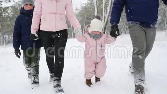 穿着暖身连衣裙的宝宝在做第一步孩子学会走路友好的全家人在冬季森林散步度假视频的预览图
