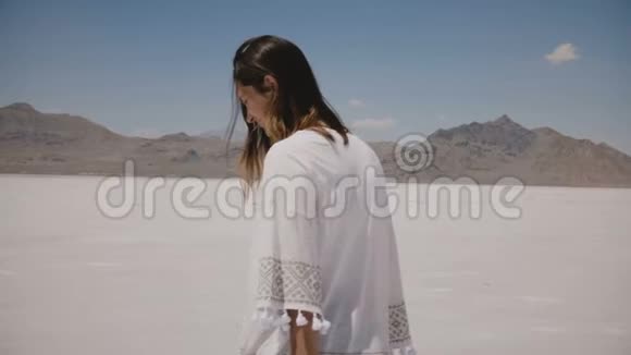 镜头跟随美丽的年轻快乐的女人看着镜头双臂张开在犹他州的盐漠湖旋转视频的预览图