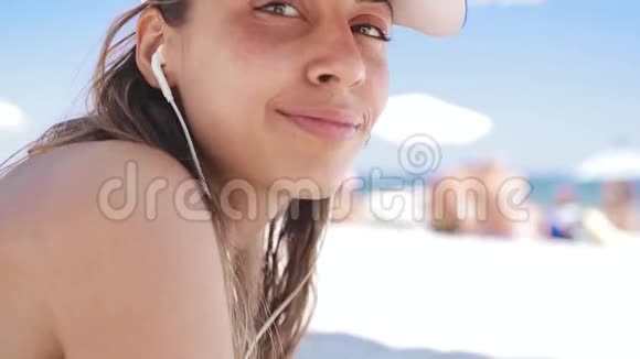 在沙滩上躺着一位美丽的晒黑的微笑女子的特写肖像她躺在白沙上放松地听着音乐视频的预览图