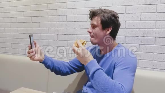 男人在咖啡馆里吃汉堡包在手机上自拍视频的预览图