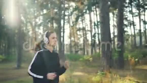漂亮的女孩在公园慢跑在空闲时间用耳机欣赏音乐现代技术青年文化和视频的预览图