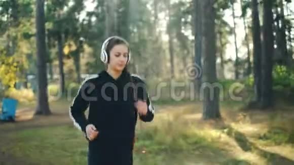 在公园里慢跑和听音乐的迷人女人的多莉镜头通过耳机欣赏歌曲和身体视频的预览图