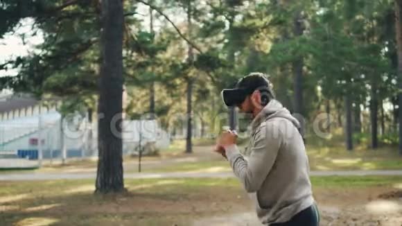 戴着虚拟现实眼镜的年轻人独自在公园里锻炼戴着耳机和移动的手臂就像在打架一样视频的预览图