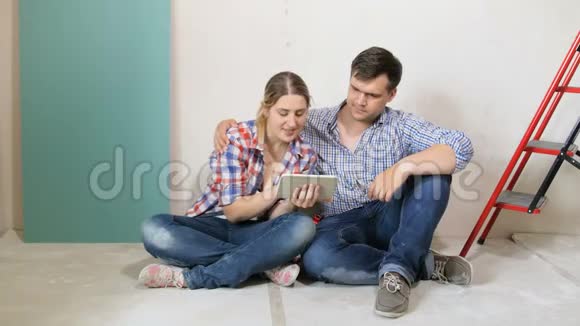 年轻家庭为他们的新房子选择新家具的4K镜头一对坐在地板上用平板电脑视频的预览图