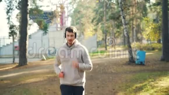 学生在公园慢跑的肖像用耳机听音乐有时看相机他穿着视频的预览图
