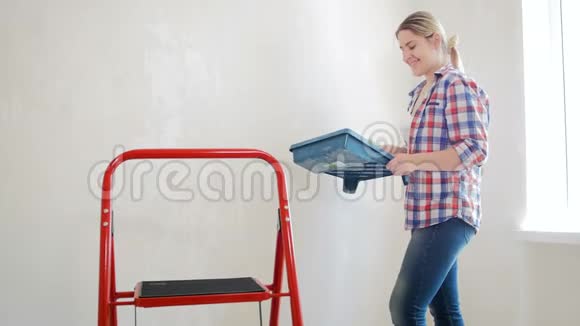 4k视频年轻女子拿着调色板用油漆滚筒在她的房子里粉刷墙壁视频的预览图