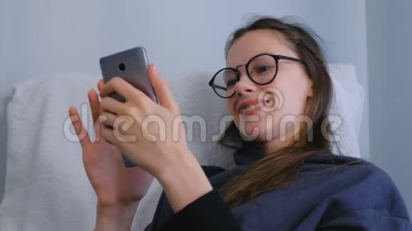 快乐的女人戴着眼镜在智能手机上浏览和寻找社交媒体视频的预览图