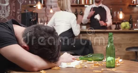 喝醉酒的顾客睡在木制的脏桌子上视频的预览图