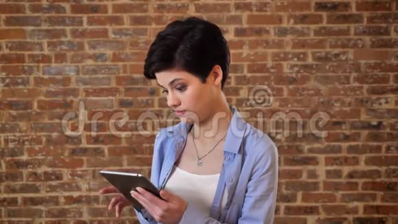 年轻漂亮的女孩正在玩她的平板电脑娱乐通信概念砖背景视频的预览图
