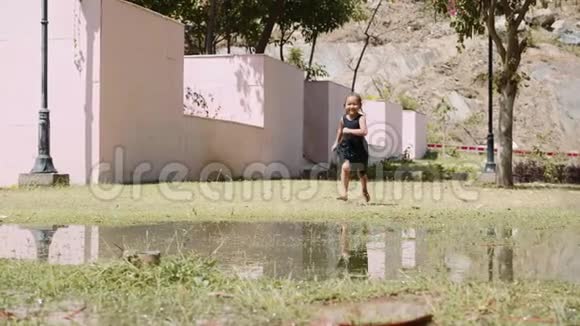 快乐的女孩正在绿色草坪上的水坑上缓慢地奔跑视频的预览图