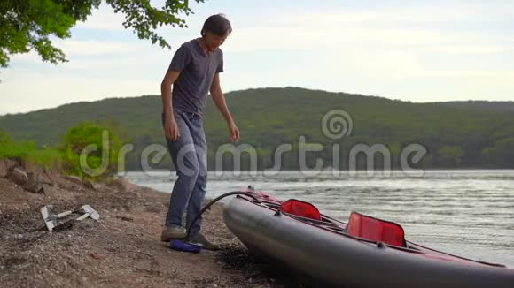 年轻人给他的皮艇充气准备在湖中划水慢镜头视频的预览图