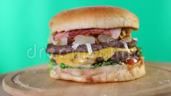 带有奶酪酱汁和蔬菜的大汉堡在绿色屏幕背景前的木板上快速旋转视频的预览图