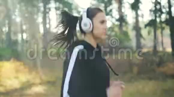 美丽的年轻女士戴着耳机在公园慢跑听音乐享受活动和最喜欢的歌曲视频的预览图
