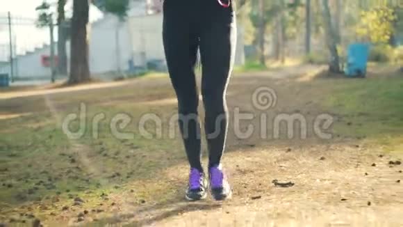 穿着运动鞋和运动服的漂亮年轻女士戴着耳机在公园慢跑享受身体健康视频的预览图