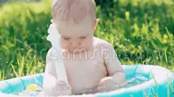 夏天小男孩在草坪上的充气游泳池里玩水溅视频的预览图