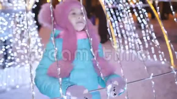 晚上在圣诞集市上的小女孩在彩灯和花环中度过了快乐而有趣的假期视频的预览图