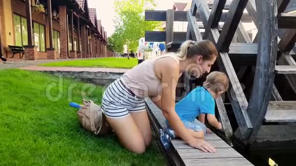 4k视频快乐微笑幼儿男孩与年轻的母亲在运河旁边的旧水磨轮视频的预览图