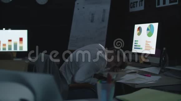疲倦的商人睡在黑暗的办公室里的工作桌前电脑上视频的预览图