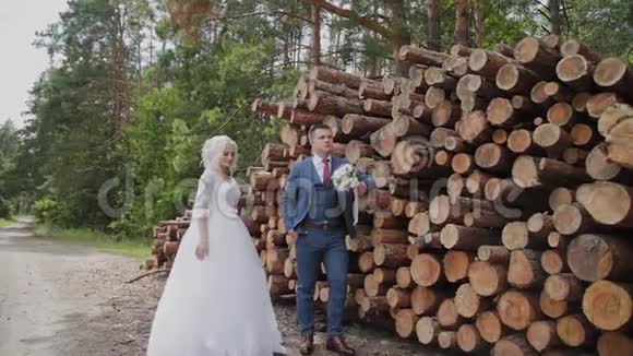 美丽的新郎和金发新娘在森林里的原木旁边拥抱和亲吻视频的预览图