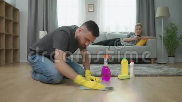 疲惫的男人打扫地板女人用智能手机躺在沙发上视频的预览图