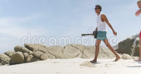 在海滩上携带冰盒的混血男性朋友的侧面景色视频的预览图