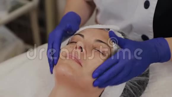 专业美容师用擦洗油涂在女人的脸上用她的手按摩视频的预览图
