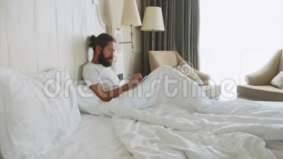 一个大胡子的年轻人在家里的卧室里醒来后在写日记视频的预览图
